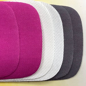 May include: Three fabric patches in different colors: pink, white, and gray. The patches are oval-shaped and have a textured surface.