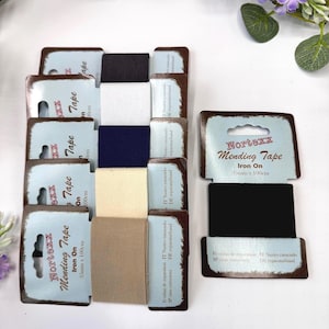 May include: A collection of Nortexx iron-on mending tape rolls in various colors including black, white, navy, cream, and beige. Each roll is mounted on a light blue cardboard backing with the text Nortexx Mending Tape 35mm x 100cm printed.
