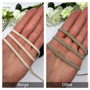 May include: Two spools of elastic cord, one beige and one olive green. The elastic cord is shown wrapped around a hand.