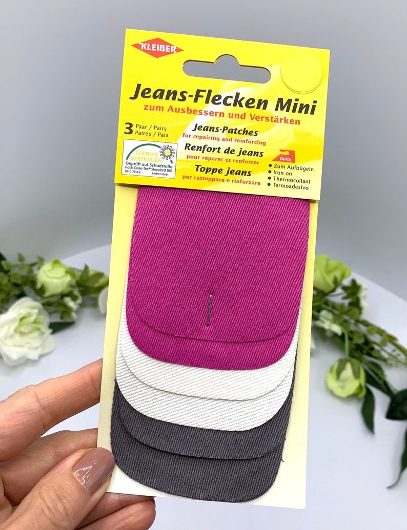 May include: A pack of three denim patches for repairing and reinforcing jeans. The patches are in pink, white, and gray. The packaging says "Jeans-Flecken Mini" and "Quick".