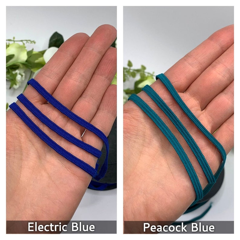 May include: Two strands of elastic cord, one electric blue and one peacock blue, are held in a hand. The cords are approximately 1/4 inch wide.