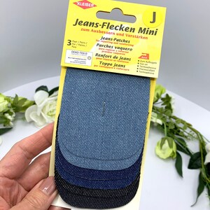 May include: A pack of three denim patches for repairing and reinforcing jeans. The patches are in different shades of blue and black. The packaging is yellow and has the text "Jeans-Flecken Mini" and "zum Ausbessern und Verst&auml;rken".