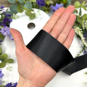 May include: A close-up of a black satin ribbon held in a hand. The ribbon is smooth and shiny.