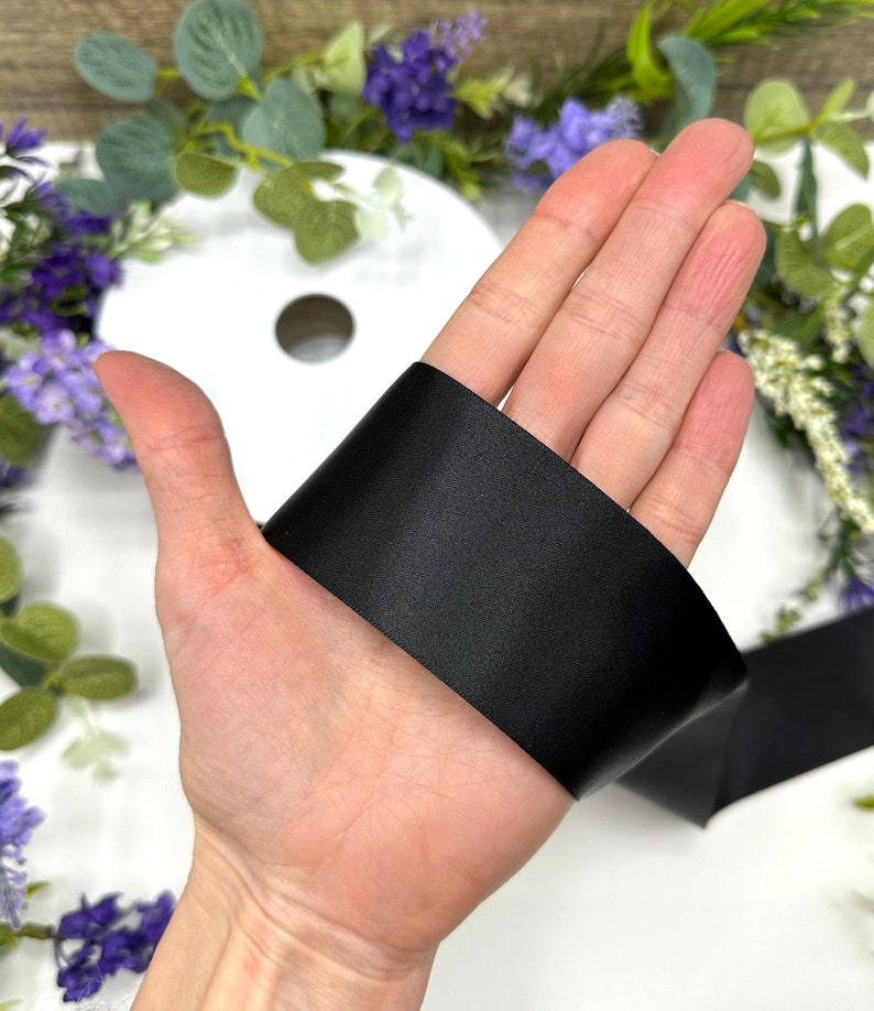 May include: A close-up of a black satin ribbon held in a hand. The ribbon is smooth and shiny.