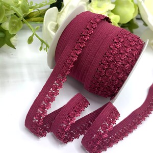Puede incluir: Una bobina de cinta el&aacute;stica de color burdeos con un delicado patr&oacute;n floral. La cinta tiene aproximadamente 2,5 cm de ancho y una textura suave y el&aacute;stica.
