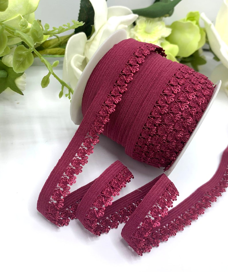 Puede incluir: Una bobina de cinta el&aacute;stica de color burdeos con un delicado patr&oacute;n floral. La cinta tiene aproximadamente 2,5 cm de ancho y una textura suave y el&aacute;stica.