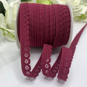Puede incluir: Un rollo de encaje el&aacute;stico de color burdeos con borde festoneado. El encaje tiene un delicado patr&oacute;n floral.