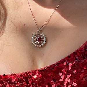 May include: A woman wearing a red sequin strapless dress with a silver necklace featuring a red gemstone compass pendant.