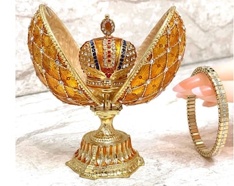 May include: A gold-tone jeweled egg with a crown on top, open to reveal an empty interior. A gold-tone bracelet with clear stones is shown next to the egg.