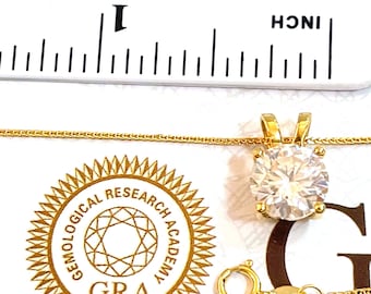 Può includere: Una collana con catena d'oro con un grande ciondolo rotondo di pietra preziosa trasparente. Il ciondolo è incastonato in una montatura d'oro e ha una piccola chiusura dorata. La collana è accompagnata da un piccolo cartellino dorato con il testo "Gemological Research Academy GRA".