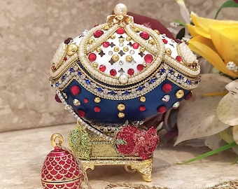 May include: A blue and white jeweled egg-shaped music box with a gold stand and a red jeweled egg pendant on a gold chain.