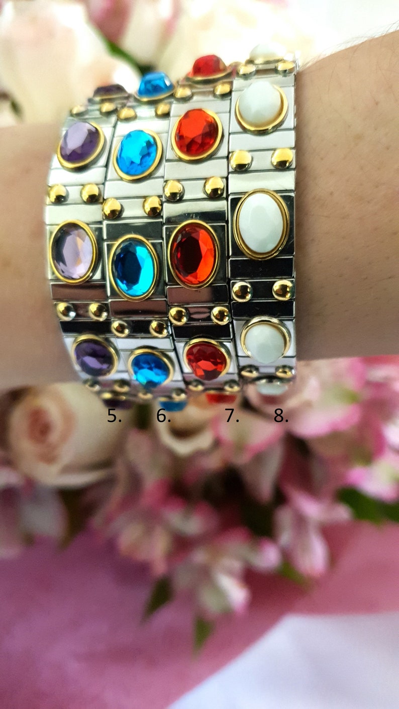 May include: A stack of four bracelets featuring different coloured gemstones. The bracelets are made of silver metal with gold accents. The gemstones are purple, blue, red, and white.