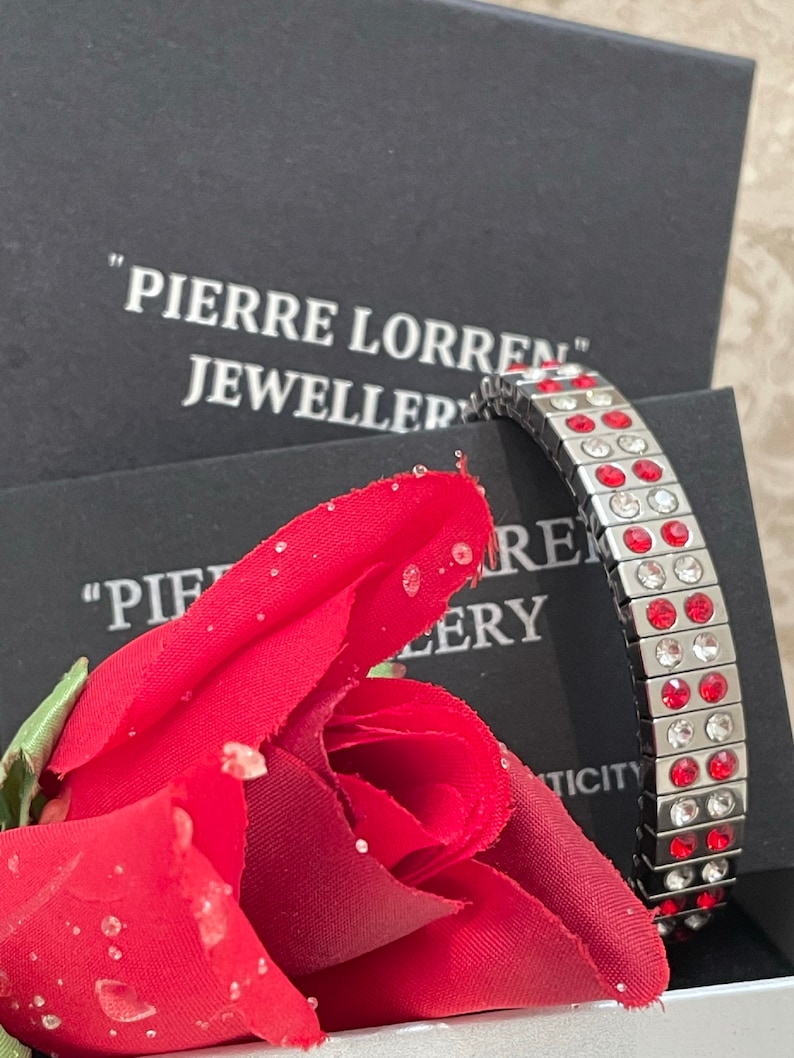 May include: A silver magnetic bracelet with red and clear crystals. The bracelet is in a black box with the text "Pierre Lorren Jeweller" on the box.