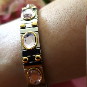 May include: A silver and gold bracelet with a row of oval-shaped pink gemstones. The bracelet is made of linked metal pieces.