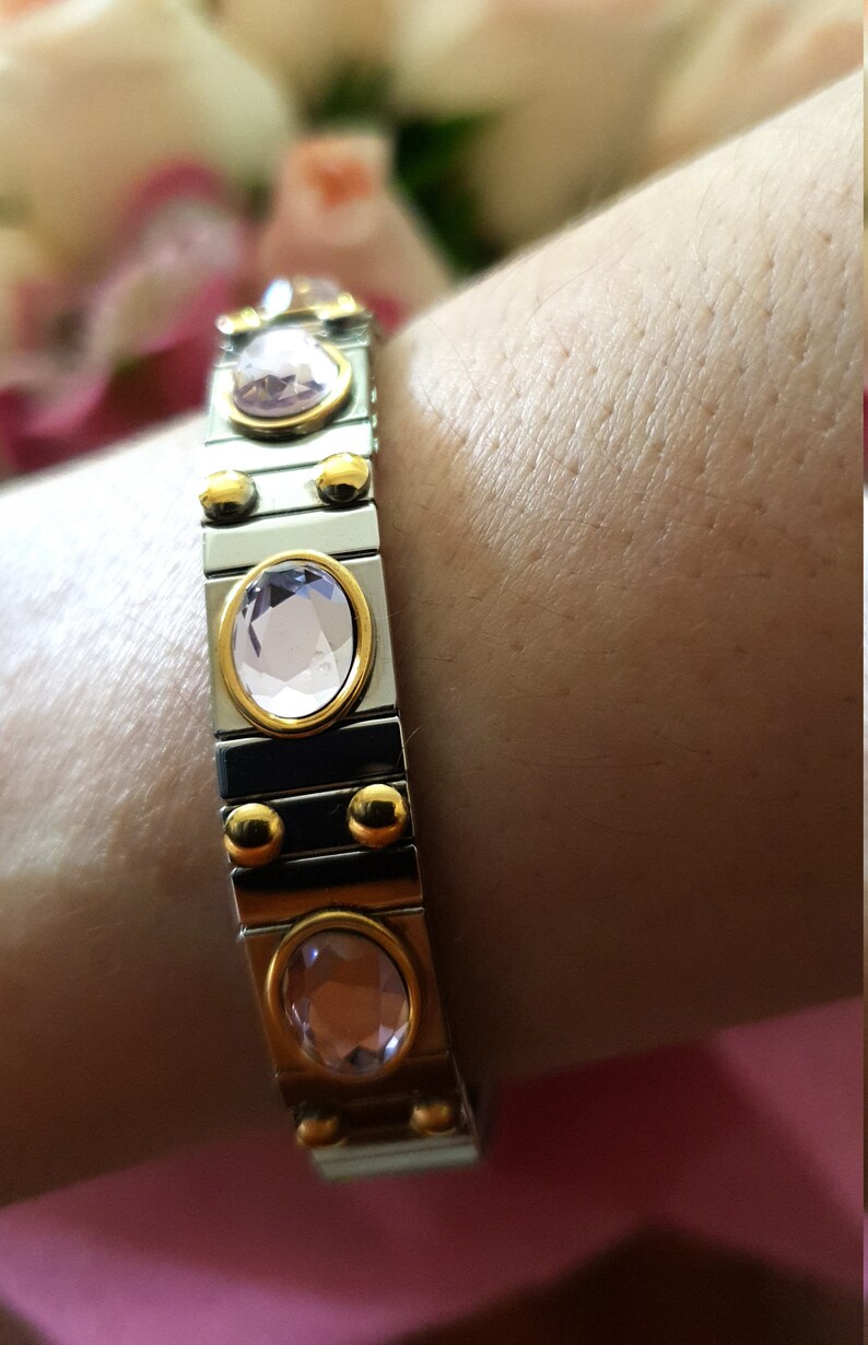 May include: A silver and gold bracelet with a row of oval-shaped pink gemstones. The bracelet is made of linked metal pieces.