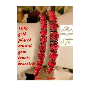 May include: Two gold-plated tennis bracelets with red crystal gems. The bracelets are 6mm and 8mm wide.  18kt gold plated crystal gem tennis bracelets.