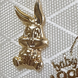 May include: A gold-colored Bugs Bunny charm. The charm is three-dimensional and shows Bugs Bunny sitting down with his hands in his lap.