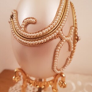 May include: A white porcelain egg with gold and pearl accents. The egg is on a gold stand with three legs.