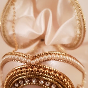 May include: A white egg-shaped trinket box with a gold and pearl trim. The box is open and the inside is lined with white satin.