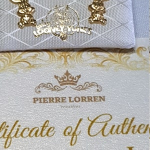 May include: A white certificate of authenticity for a pair of 18kt gold earrings featuring a Bugs Bunny design. The certificate is from Pierre Lorren.