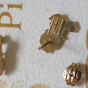 May include: A pair of gold-tone earrings featuring a small, detailed design. The earrings are marked with the text "James Avery &copy; 2011".