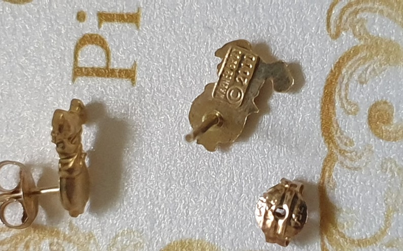 May include: A pair of gold-tone earrings featuring a small, detailed design. The earrings are marked with the text "James Avery &copy; 2011".