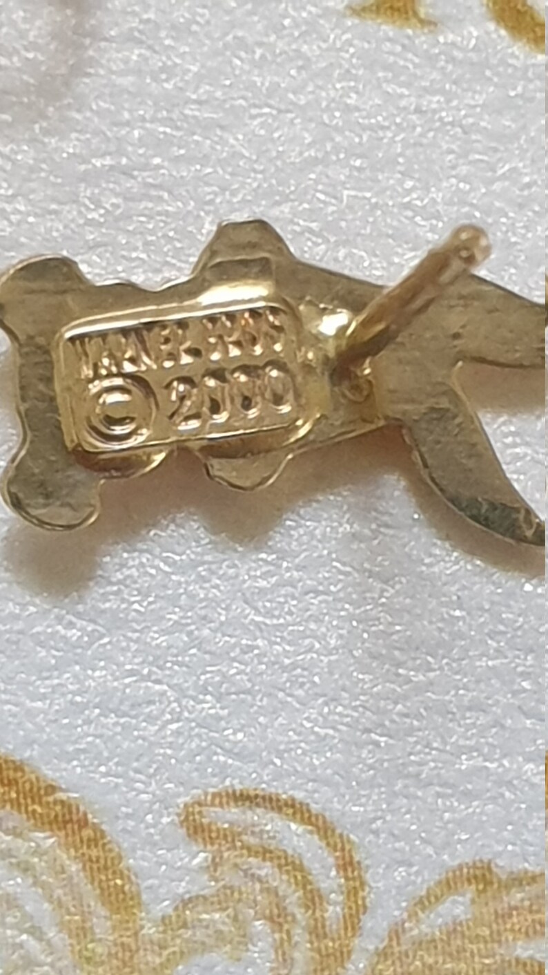 May include: Gold-toned metal earrings with a stylized design. The earrings have a post back closure and are marked "JAPAN 2100".