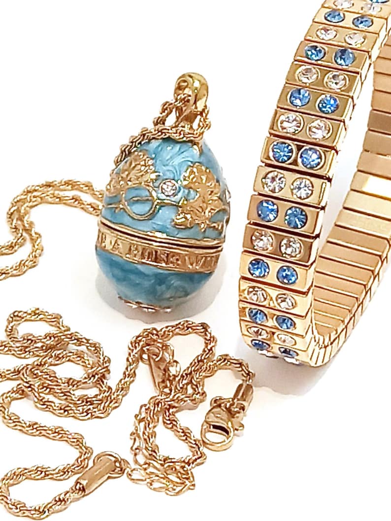 Puede incluir: Un collar de cadena de oro con un colgante de huevo azul y dorado y una pulsera de oro con cristales azules y transparentes.