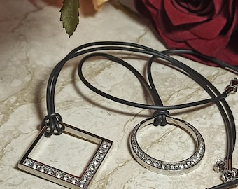 May include: A silver necklace with a square and a circle pendant, both adorned with clear rhinestones. The necklace is on a black cord.