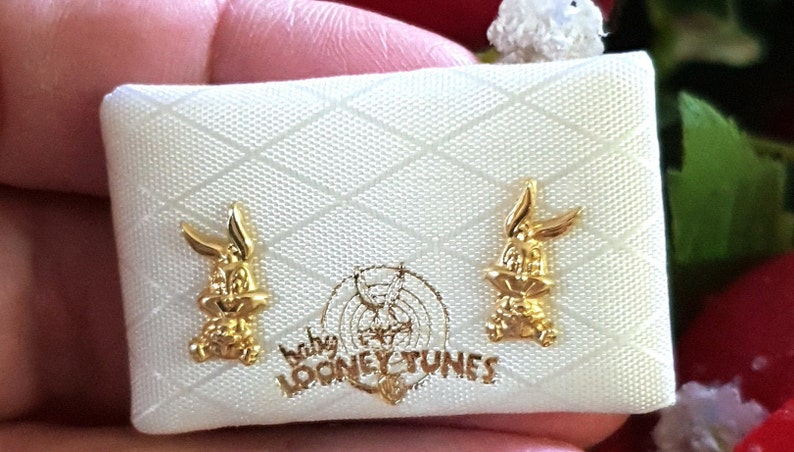 May include: A white box with a gold Bugs Bunny design. The box has the words "Baby Looney Tunes" printed on it. The box contains a pair of gold Bugs Bunny earrings.