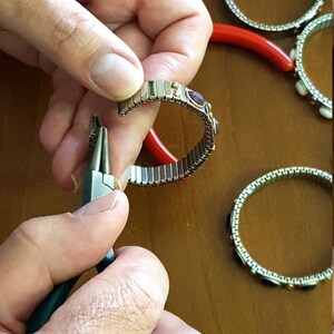 May include: A person is using pliers to close a silver bracelet with small, colourful gemstones. The bracelet is made of linked metal pieces.