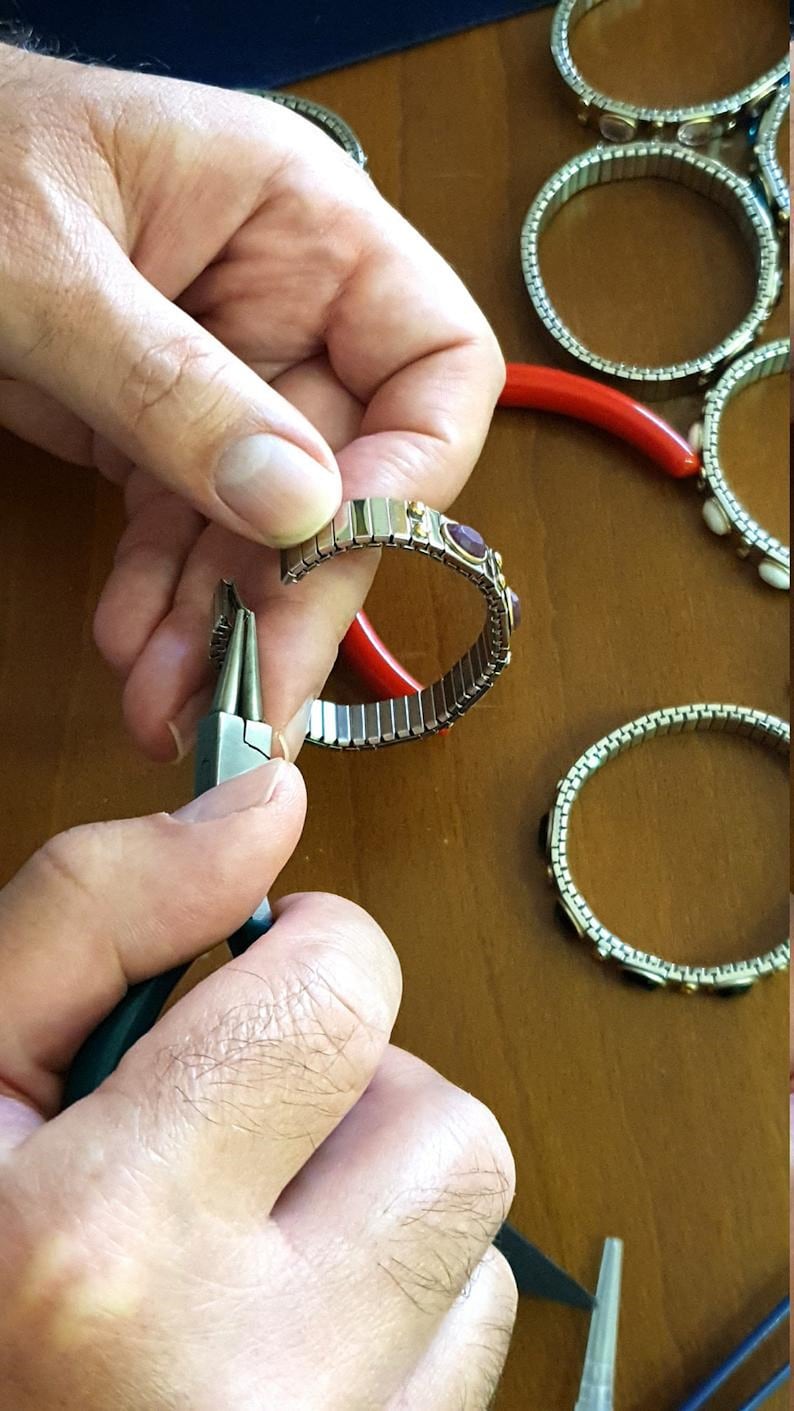 May include: A person is using pliers to close a silver bracelet with small, colourful gemstones. The bracelet is made of linked metal pieces.