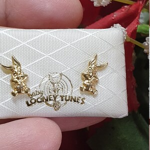 May include: A pair of gold-colored Bugs Bunny earrings in a white box with the words "Looney Tunes" printed on it.