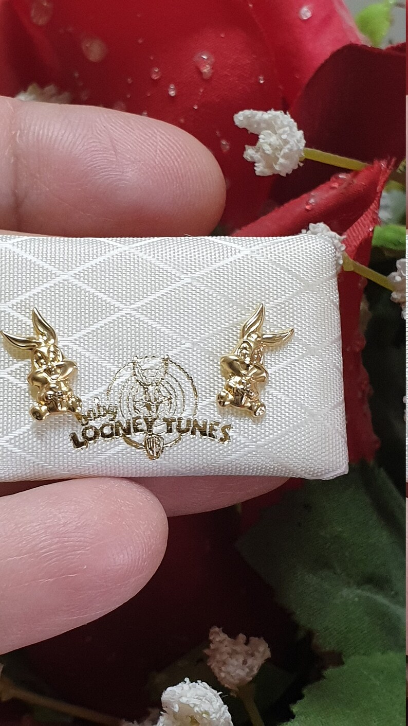 May include: A pair of gold-colored Bugs Bunny earrings in a white box with the words "Looney Tunes" printed on it.