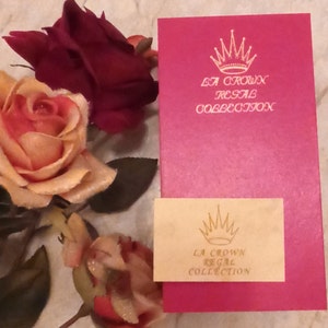 May include: A pink box with a gold crown and the text "La Crown Regal Collection" on the front. A smaller, cream-colored box with the same logo is in front of the pink box.
