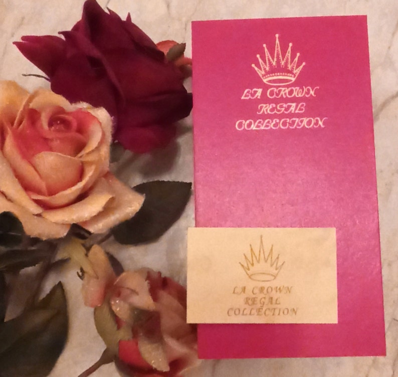 May include: A pink box with a gold crown and the text "La Crown Regal Collection" on the front. A smaller, cream-colored box with the same logo is in front of the pink box.