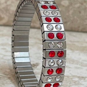 May include: A silver bracelet with a stretchy band and alternating rows of red and clear rhinestones.