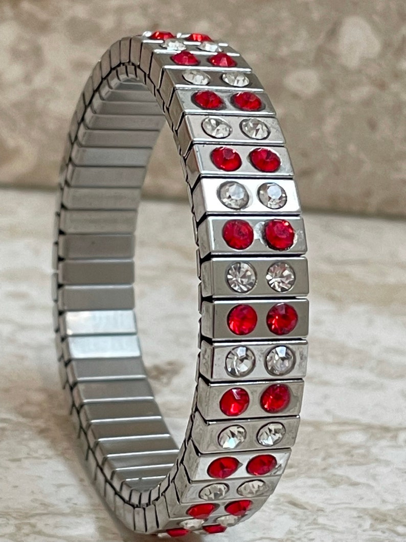 May include: A silver bracelet with a stretchy band and alternating rows of red and clear rhinestones.
