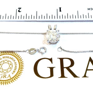 Puede incluir: Un collar de cadena de plata con un gran colgante redondo de piedra preciosa transparente. El colgante está engastado en un engaste de garras de plata. El collar mide 45,7 cm de largo y se muestra junto a una regla para referencia de tamaño. El collar viene acompañado de un certificado de autenticidad de la Gemological Research Academy (GRA).
