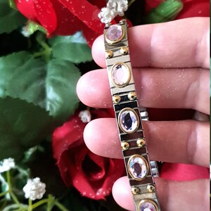 May include: A silver and gold bracelet with pink oval-shaped gemstones. The bracelet is made of linked metal pieces.