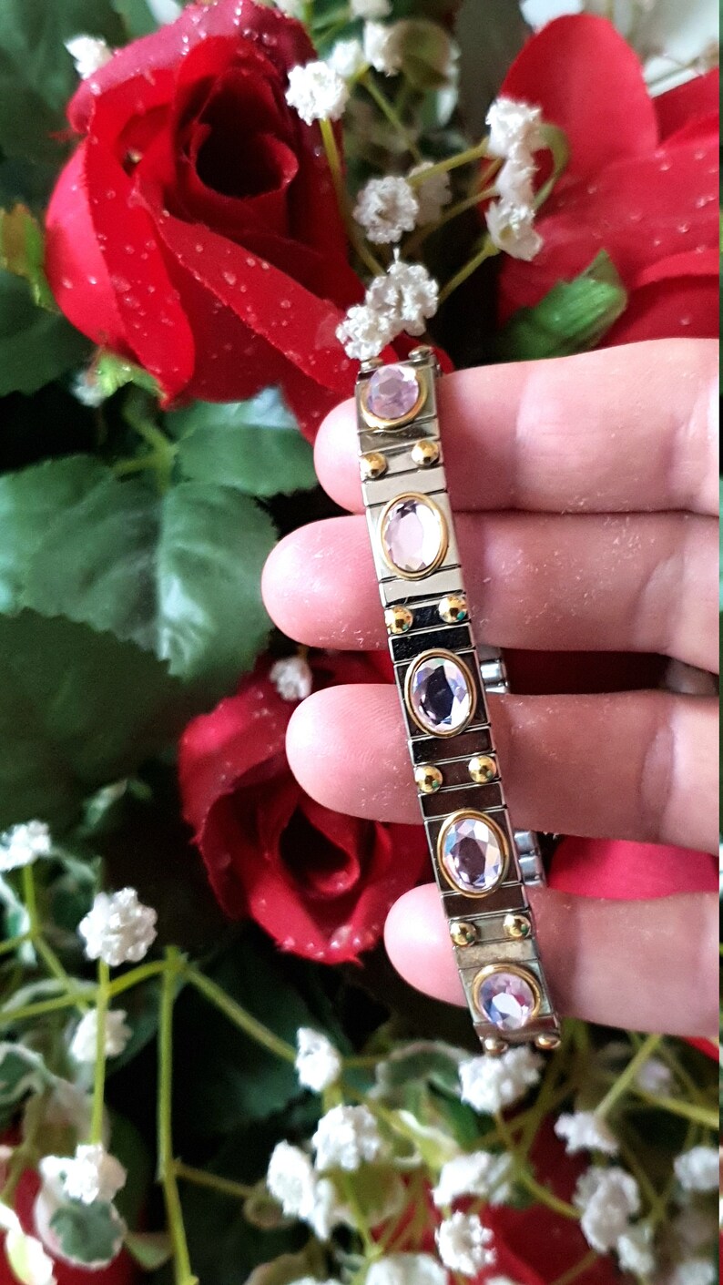 May include: A silver and gold bracelet with pink oval-shaped gemstones. The bracelet is made of linked metal pieces.