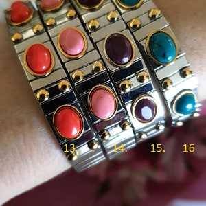 May include: Four silver bracelets with colourful oval-shaped stones. The bracelets are numbered 13, 14, 15, and 16.