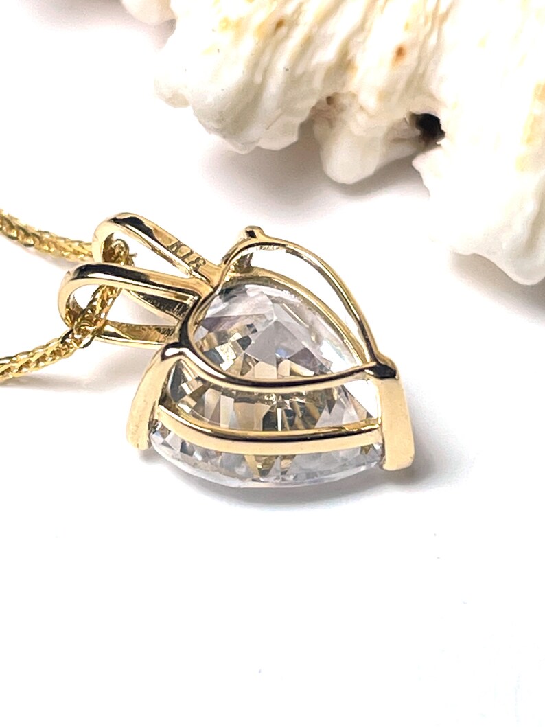 Pu&ograve; includere: Un ciondolo a forma di cuore in oro con una pietra di cristallo trasparente. Il ciondolo &egrave; su una catena d'oro.