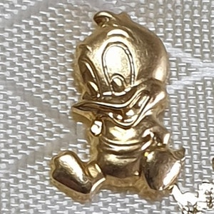 May include: A gold-colored cartoon duck figurine. The duck is standing on its two feet and has its wings spread out. The duck has a mischievous expression on its face.