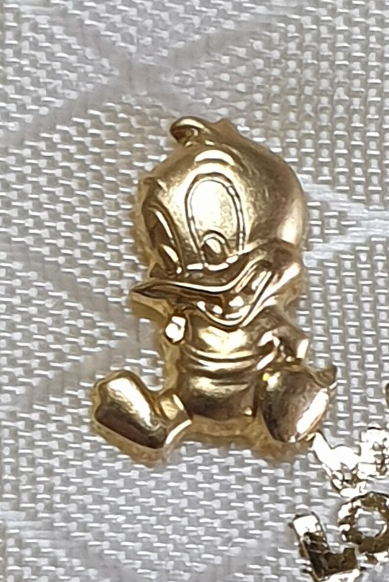 May include: A gold-colored cartoon duck figurine. The duck is standing on its two feet and has its wings spread out. The duck has a mischievous expression on its face.