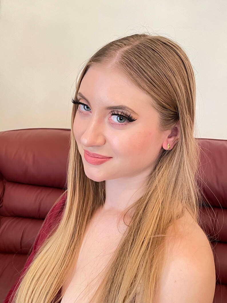 May include: A young woman with long, straight blonde hair is smiling at the camera. She is wearing a red top and has her hair pulled back from her face.
