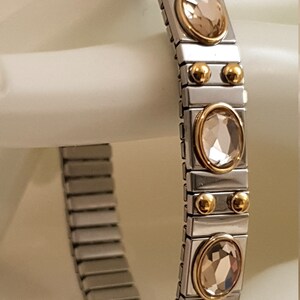 May include: A silver and gold bracelet with a stretchy band and round, clear crystals.