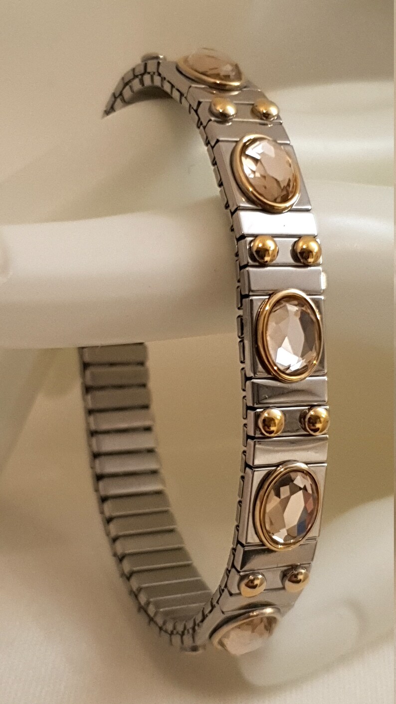 May include: A silver and gold bracelet with a stretchy band and round, clear crystals.