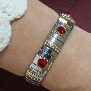 May include: A silver and gold bracelet with red gemstones and clear rhinestones. The bracelet is made of linked metal pieces.