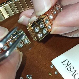 Puede incluir: Un brazalete dorado con una fila de cristales transparentes. El brazalete se est&aacute; ensamblando con pinzas y cristales sueltos.